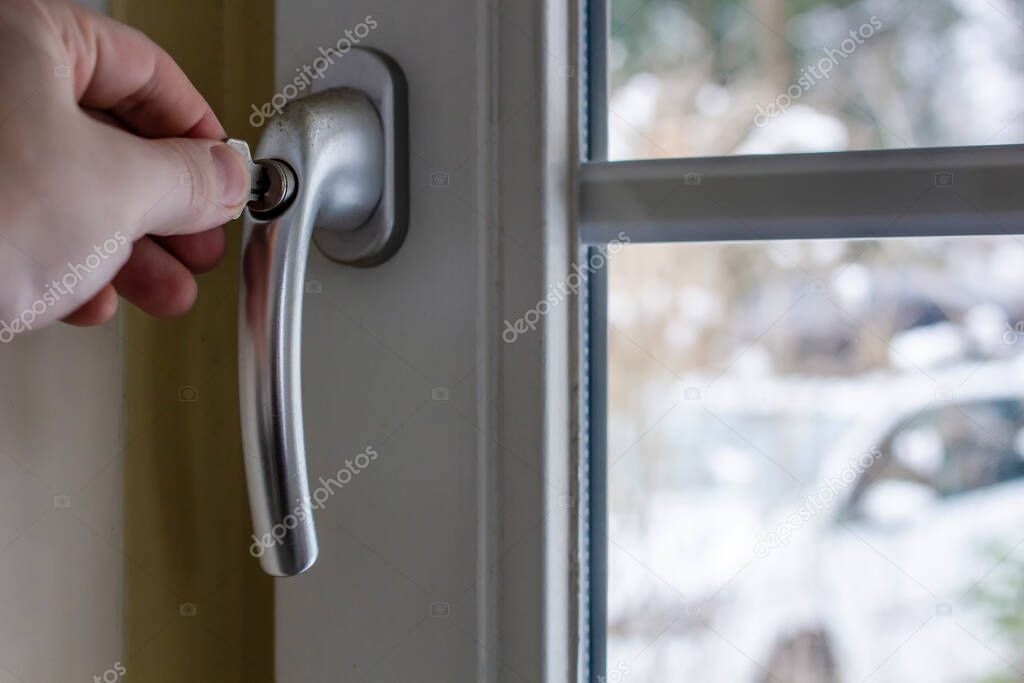The concept of child safety, protection of the child falling out of the window. Male hand closes the key lock on the handle on the PVC window. Close-up.