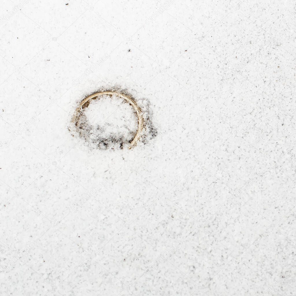 The gold wedding ring, a symbol of love and loyalty, thrown out after the divorce, lonely and sadly lies in a snowdrift, in cold winter. The concept of separation of lovers. Close-up.