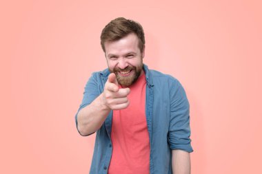 Sakallı bir adam onun önünde parmağını gösteriyor ve kasıtlı olarak birine gülüyor. Mercan zemininde izole edilmiş. Yakın plan.