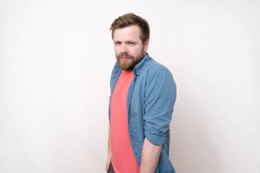 Utangaç, aşık bir adam omuzlarını kaldırdı, ellerini cebine koydu ve dikkatlice baktı, gülümsedi. Beyaz yakutta izole edilmiş. Yakın plan..