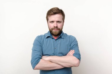 Memnun sakallı bir adam kollarını kavuşturup dikkatle bakar. Beyaz arka planda izole edilmiş. Yakın plan.