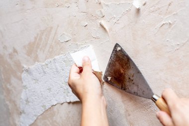 Odanın tamiri sırasında duvardaki eski duvar kağıdını bir spatulayla sökün. Yakın plan..