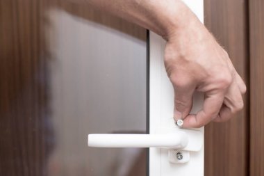 Bir adam elinde metal bir vida tutuyor ve bu vidayla bir PVC penceresine tutunacak. Yakın plan..