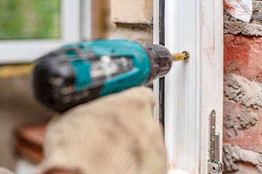 Erkek eller elektrikli tornavida ve vida kullanarak bir PVC pencere çerçevesini tuğla duvara asacaklar. Yakın plan.