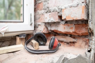 İş kulaklıkları, PVC penceresinin yanındaki tuğla duvarda duran gürültüye karşı korur. Metal-plastik inşaat işlemi. Yakın plan..
