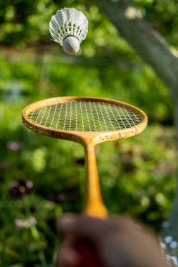 Bir el, bir badminton raketini tutuyor ve bulanık yeşil bir arka planda, bir mekik çükünü fırlatıyor, bir yaz gününde. Yakın plan..