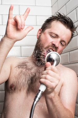 Sakallı bir adam banyoda şarkı söyler, mikrofon yerine akan suyla duş alır ve rock n roll işareti gösterir ya da şeytan boynuzu hareketi yapar. Yakın plan..