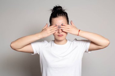 Güzel kadın elleriyle gözlerini kapatır. Beyaz arka planda izole edilmiş. Yakın plan..