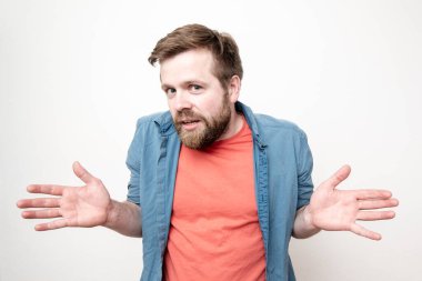 Genç, sakallı bir adam omuzlarını silkiyor avuçlarını uzatıyor ve masum gözlerle kameraya bakıyor. Beyaz arkaplanda izole.