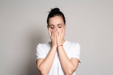 Şok olmuş, üzgün genç bir kadın iki eliyle ağzını kapadı. Beyaz bir arkaplanda izole edilmiş.