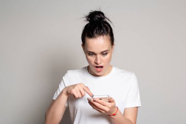 Şok olmuş genç bir kadın akıllı telefonuna bakar, kötü haberleri ya da fotoğrafları görür, ağzını korku ve şaşkınlık içinde açar ve parmağını telefona doğrultur. Duygu, ifade.