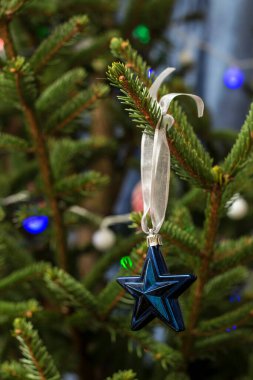Güzel mavi oyuncak, bulanık bir arka planda çelengi olan bir Noel ağacında kurdelesi olan bir yıldız..