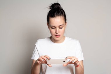 Çekici kadın ilginç bir şekilde haberleri akıllı telefondan izliyor. Gri bir arkaplanda izole edilmiş.