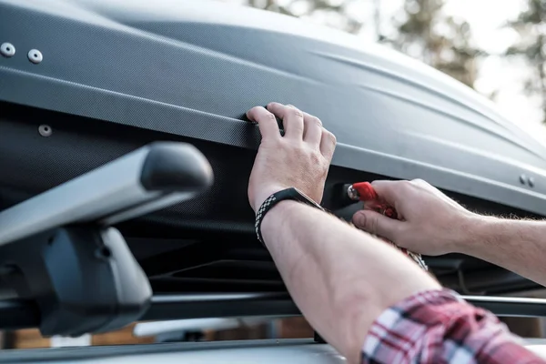 Erkek elleri, aile tatiline çıkmadan önce arabanın çatısındaki geniş bagaj ya da kargo kutusunu koruyor. Yakın plan..