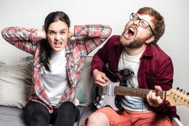 Sakallı erkek besteci altı telli elektro gitar çalar ve yüksek sesle kendi bestesinden bir şarkı söyler, kız arkadaşı bu müzikten hoşlanmaz, kulaklarını elleriyle kapatır ve dişlerini gösterirdi..