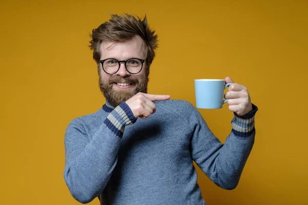 Divertido, hombre feliz señala el dedo índice a una taza de bebida caliente, ofreciéndoselo a amigos . — Foto de Stock