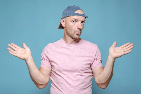 Man with an innocent expression on face spreads arms to the sides and looks at the camera in bewilderment. Blue background. — Stock Photo, Image