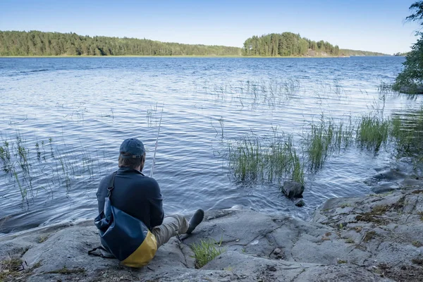 L'uomo che riposa con una borsa sigillata si siede vicino al lago sulla riva rocciosa e gode del bellissimo paesaggio. Stile di vita. — Foto Stock