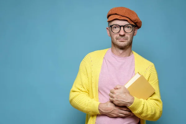 Rustige, enigszins bezorgde man in heldere kleren houdt een boek in handen en kijkt naar de camera. Grappig creatief persoon. Kopieerruimte. — Stockfoto