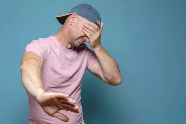 Der Mensch verweigert etwas, zeigt mit einer Hand eine Stoppgeste und schließt mit der anderen die Augen. Kopierraum. Blauer Hintergrund. — Stockfoto