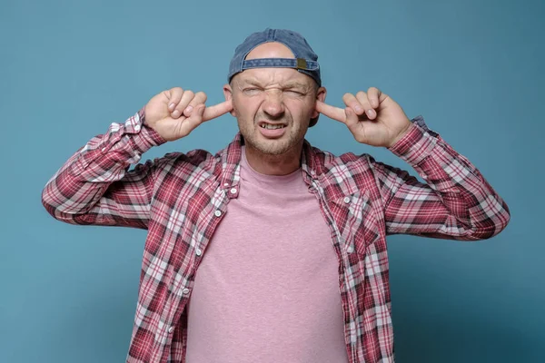 Ontevreden man bedekt oren met vingers, hij was moe van het lawaai en onaangename geluid, barst tanden en ogen. — Stockfoto