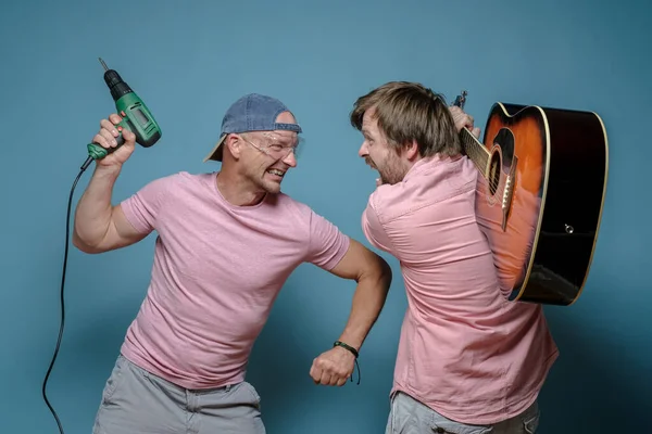 Furious musician and construction worker, they started a fight over the noise, one threatens with a drill, the other with a guitar. — Stock Photo, Image