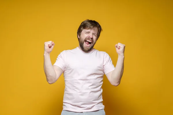 Victory. Happy bearded Caucasian man shouts joyfully and makes clenched fists up gesture. — Stock Photo, Image