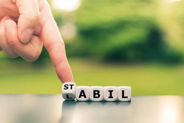 Hand turns a dice and changes the German word "labil" ("unstable — ストック写真
