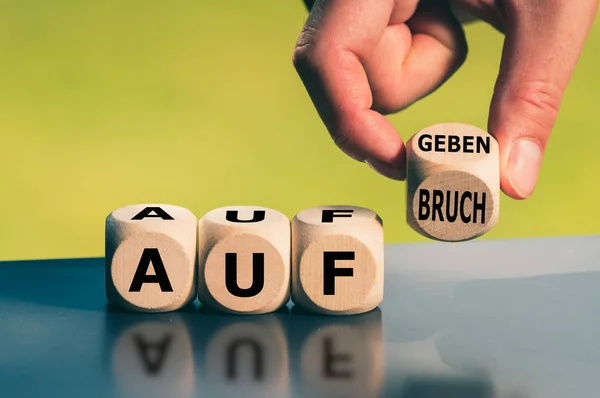 Hand turns a cube and changes the German word "Aufgeben" ("give — ストック写真
