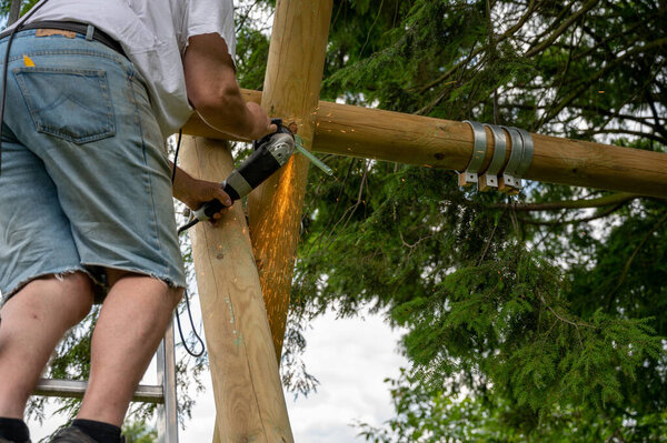 A worker is using a grinder to built a swing in a private garden.