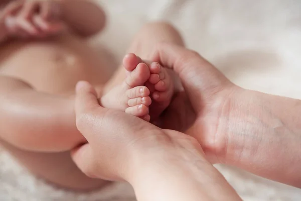 Mom holds the legs of a four-month-old baby. close up