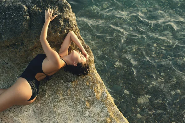 海の近くの石の上で横になっている水着でセクシーな若い女性 — ストック写真