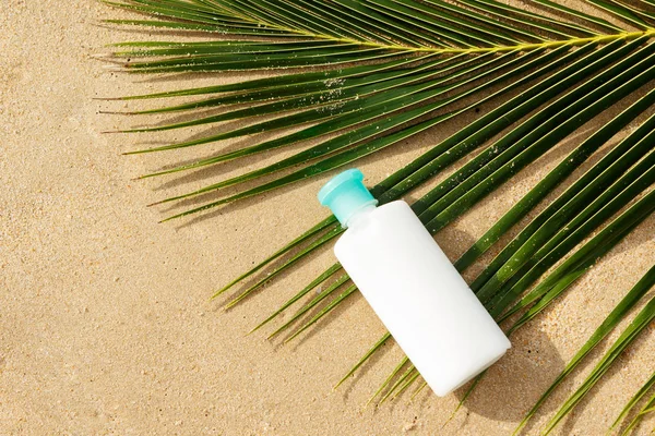 Bottle of sun protection lotion and palm leaf on the beach