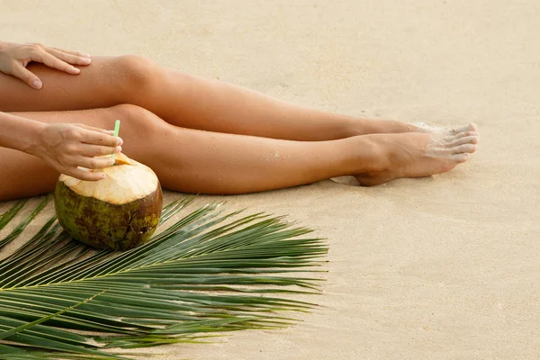 Kadın bacakları ve kumlu plajda kokteyl Hindistan cevizi
