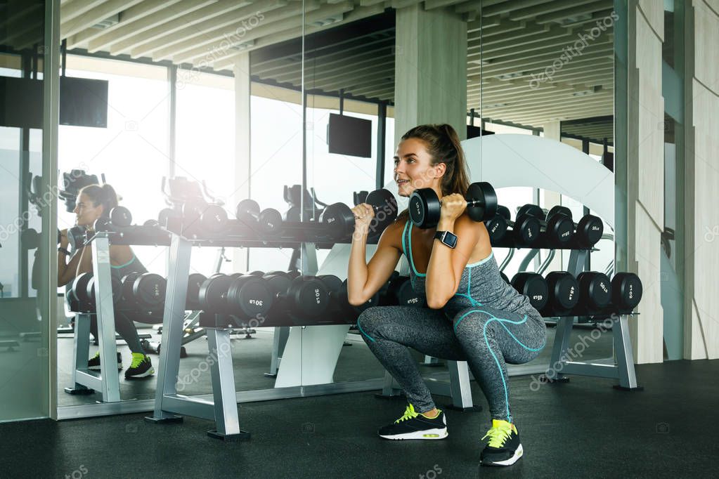 Young beautiful woman working out with dumbbells in gym