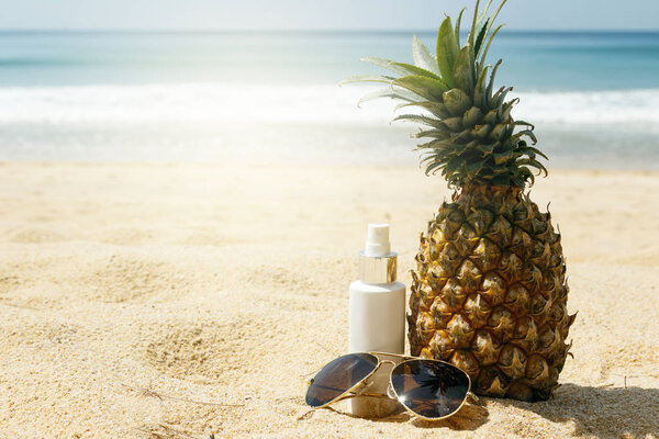 Pineapple, sunglasses and sunscreen lotion on the beach