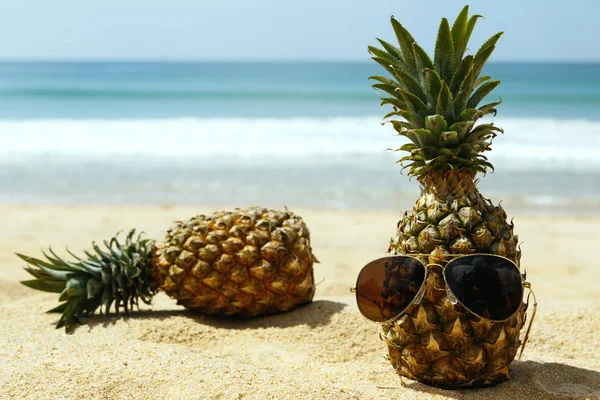 Pineapples and sunglasses on sandy beach, close up