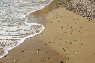 Pebble stones on sandy beach with sea wave