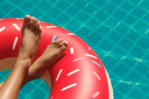 Female legs and inflatable swim ring in shape of donut in the pool