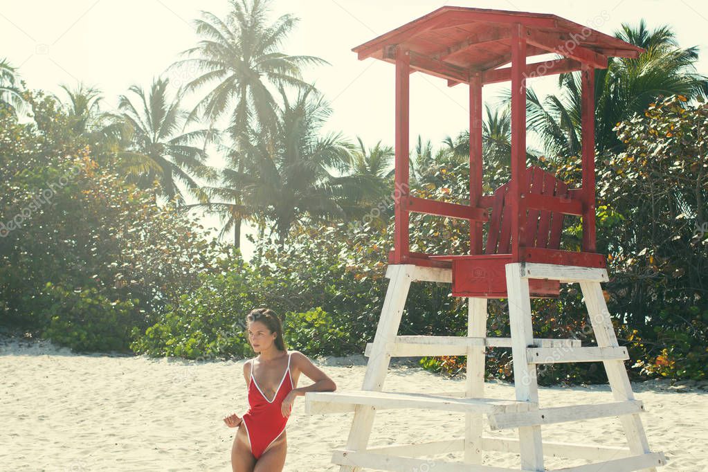 Sexy woman  in red swimsuit posing beside a lifeguard tower on the beach