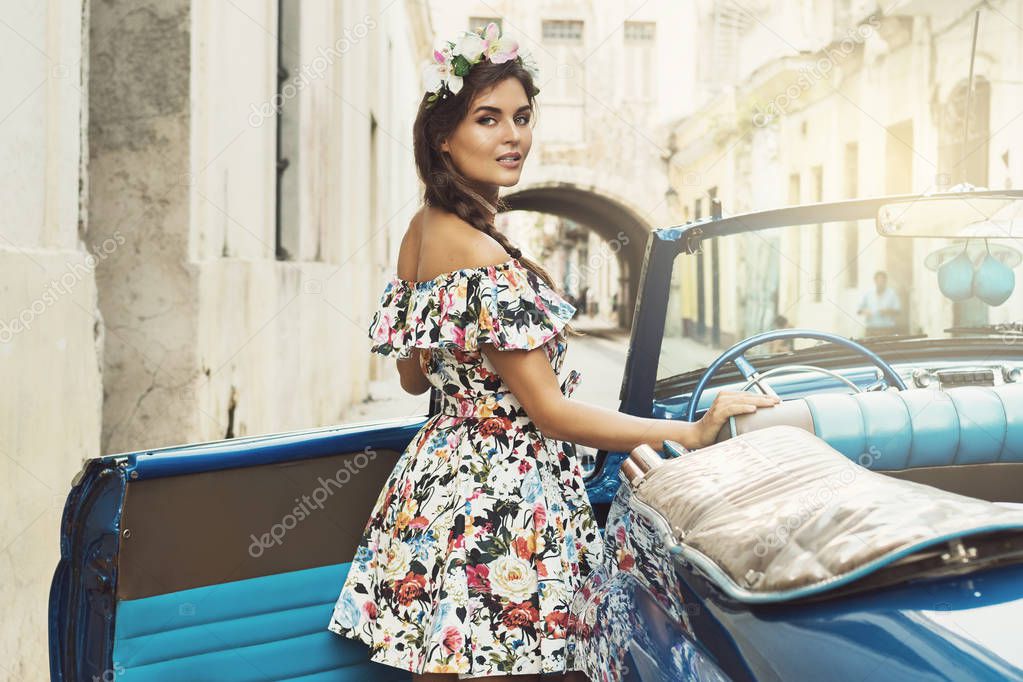 Young woman in beautiful dress beside a retro car