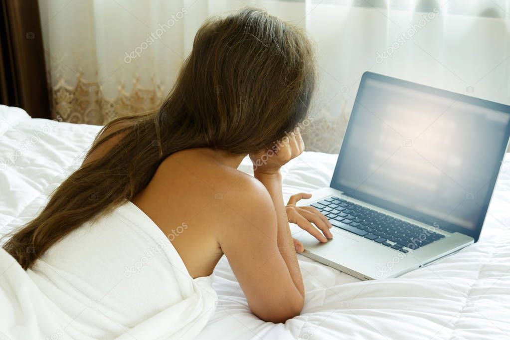 Beautiful woman lying on bed and using laptop pc