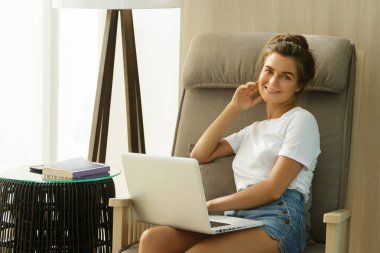 Sallanan sandalyede oturan ve dizüstü pc ile çalışan genç kadın 