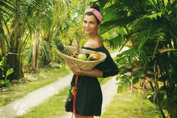 Happy young woman with basket full of exotic fruits in tropical garden