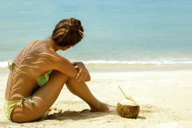 Kadın plajda palmiye yaprağı gölgesinde oturmuş ve denize bakarak