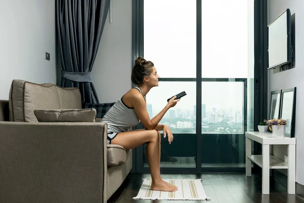 Woman sitting on couch and watching TV in modern apartment