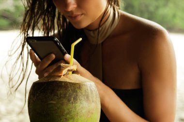 Hindistan cevizi kokteyl içme ve plaj barda smartphone kullanarak kadın
