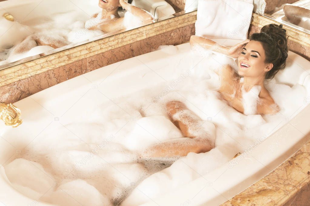 beautiful young woman taking bath with foam in luxury apartments