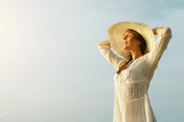Portrait of beautiful young woman with broad-brimmed hat on beach at sunset clipart