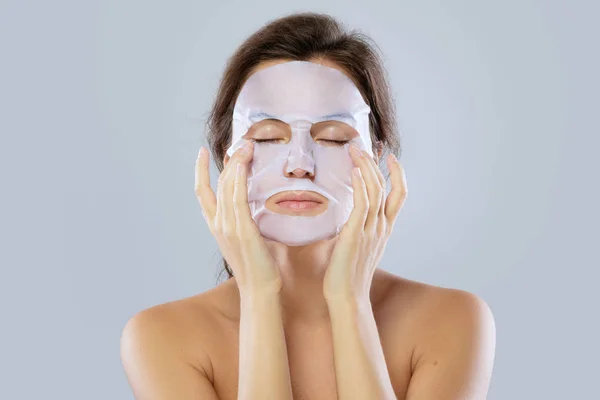面部护理和美容护理 妇女用布保湿面具在她的脸上孤立的灰色背景 — 图库照片